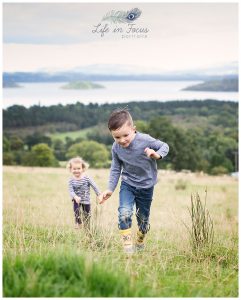 children running through field at holiday glamping site overlooking Loch Lomond Life in Focus Portraits vacation photography Luss Loch Lomond National Park Scotland