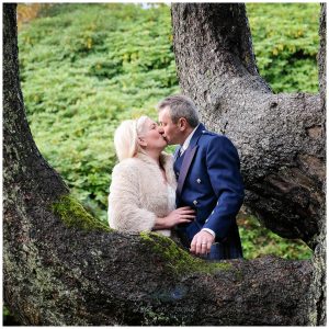 Wedding photo of bride and groom kissing under tree