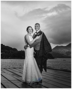 black and white photo of bride and groom on Luss pier with Ben Lomond